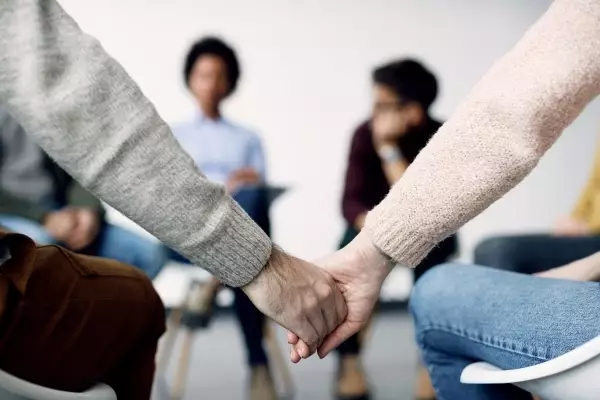 closeup-two-people-holding-hands-during-group-therapy