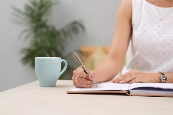 unrecognizable-woman-dress-sitting-indoors-desk-writing-journal